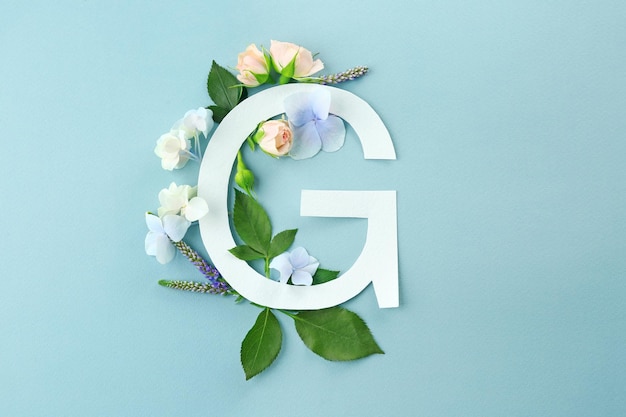 Kompozycja z literą G i pięknymi kwiatami na kolorowym tle