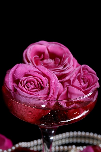 Kompozycja z różowym winem musującym i różami w szkle, na czarnym tle