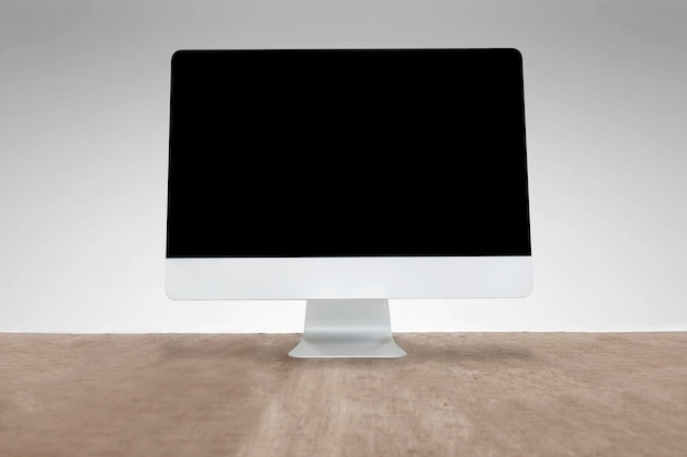Zdjęcie komputer umieszczony na biurku, szare tło na ścianie, pusty ekran do wstawiania różnych wiadomości multimedialnych