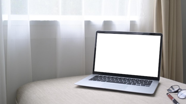Komputerowy laptop z pustym ekranem na wygodnej sofie w jasnym salonie