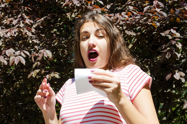 Zdjęcie koncepcja alergii kichająca młoda dziewczyna z wycieraczką do nosa wśród kwitnących drzew w parku