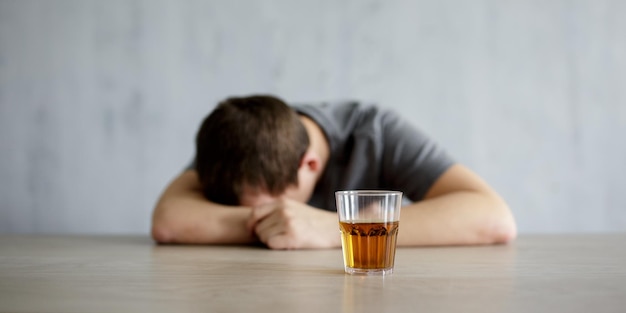 Koncepcja alkoholizmu pijany mężczyzna leżący na stole i szklanka whisky na szarej ścianie