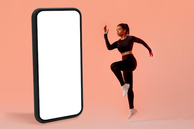Koncepcja aplikacji treningowej Szczupła dama ćwicząca w pobliżu dużego telefonu komórkowego skacząca w studio na makiecie neonowego tła