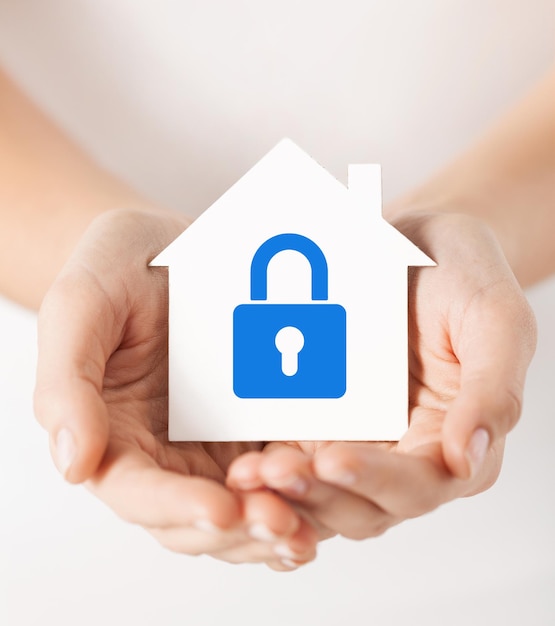 koncepcja bezpieczeństwa w domu i domu rodzinnym - zbliżenie kobiecych rąk trzymających biały papierowy dom z niebieskim zamkiem
