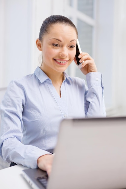 koncepcja biura, biznesu i technologii - uśmiechnięta bizneswoman z laptopem i smartfonem