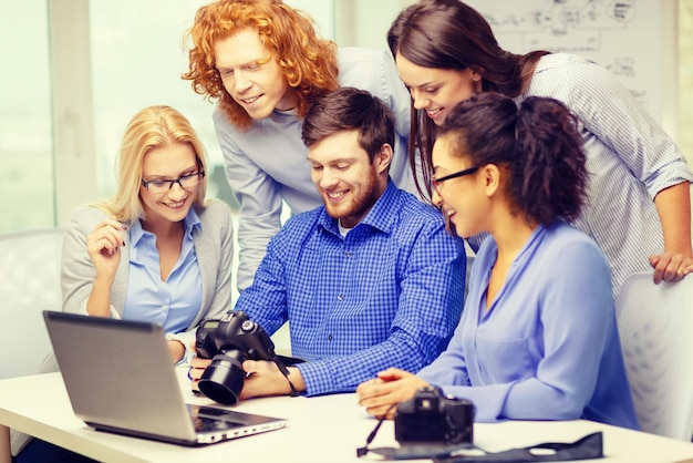 koncepcja biznesowa, biurowa i startupowa - uśmiechnięty kreatywny zespół z laptopem i aparatami fotograficznymi pracującymi w biurze