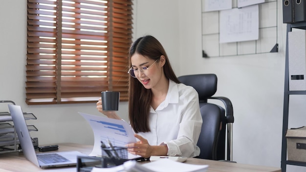 Koncepcja biznesowa Bizneswoman czyta dokument finansowy i pije kawę w nowoczesnym biurze