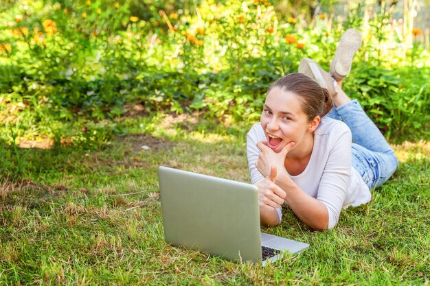 Koncepcja biznesowa freelancer. Młoda kobieta, leżąc na trawniku zielona trawa w parku miejskim pracy na komputerze typu laptop. Styl życia autentyczny szczery studentka studiująca na zewnątrz. Biuro mobilne