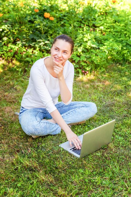 Koncepcja biznesowa freelancer. Młoda kobieta siedzi na zielonym trawniku w parku miejskim pracy na komputerze typu laptop. Styl życia autentyczny szczery studentka studiująca na zewnątrz. Biuro mobilne