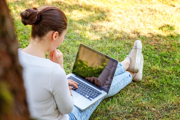 Koncepcja biznesowa freelancer. Młoda kobieta siedzi na zielonym trawniku w parku miejskim pracy na komputerze typu laptop. Styl życia autentyczny szczery studentka studiująca na zewnątrz. Biuro mobilne
