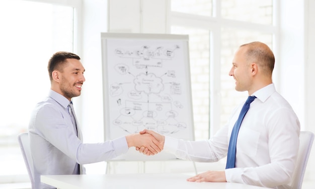 koncepcja biznesowa i biurowa - dwóch uśmiechniętych biznesmenów ściskających dłonie w biurze