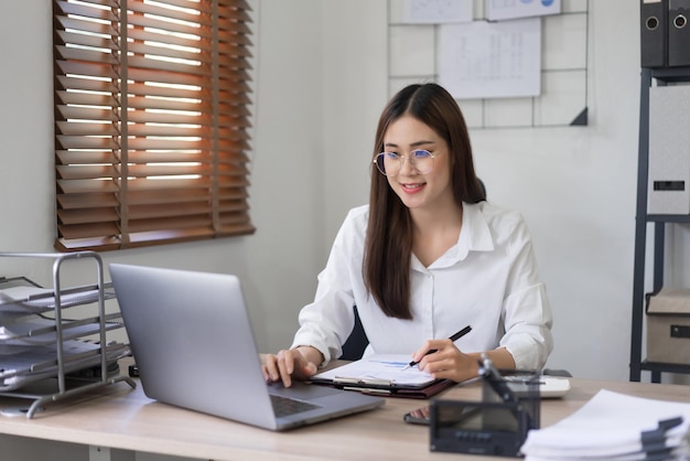 Koncepcja biznesowa Kobieta czyta dane biznesowe na laptopie i robi notatki na dokumencie
