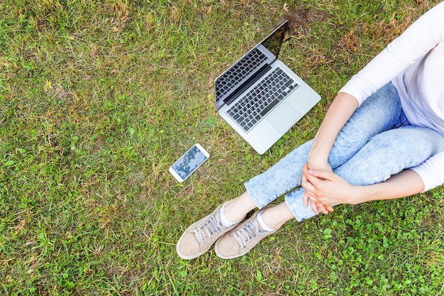 Koncepcja biznesowa niezależnego. Kobieta nogi na zielony trawnik w parku miejskim, ręce pracujące na komputerze typu laptop. Styl życia autentyczny szczery studentka studiująca na zewnątrz. Biuro mobilne