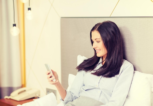 koncepcja biznesowa, technologiczna, internetowa i hotelowa - szczęśliwa bizneswoman ze smartfonem leżącym w hotelu w łóżku