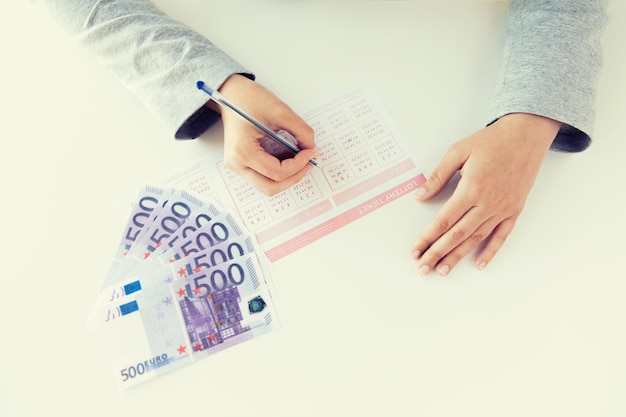 koncepcja biznesu, finansów, hazardu i ludzi - zbliżenie rąk kobiety wypełniającej los na loterię i pieniądze