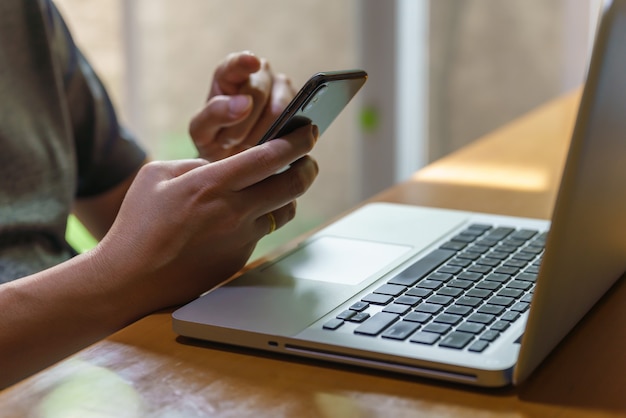 Koncepcja biznesu i technologii. Azjatycki mężczyzna trzyma i używa mobilnego smartfona z komputerem laptop.