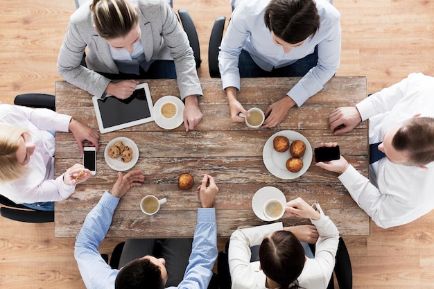 koncepcja biznesu, ludzi, przerwy i pracy zespołowej - zbliżenie kreatywnego spotkania zespołu i picia kawy z babeczkami podczas lunchu w biurze