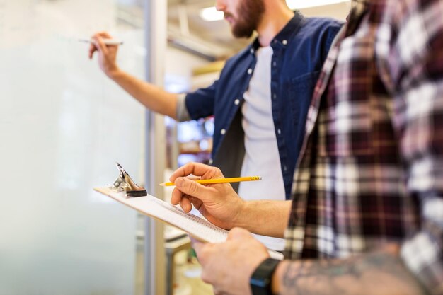 Zdjęcie koncepcja biznesu, produkcji i ludzi - mężczyźni piszący do schowka i tablicy w biurze