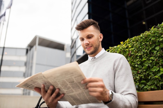 Zdjęcie koncepcja biznesu, środków masowego przekazu i ludzi - uśmiechnięty mężczyzna czytający gazetę na ławce ulicy miasta