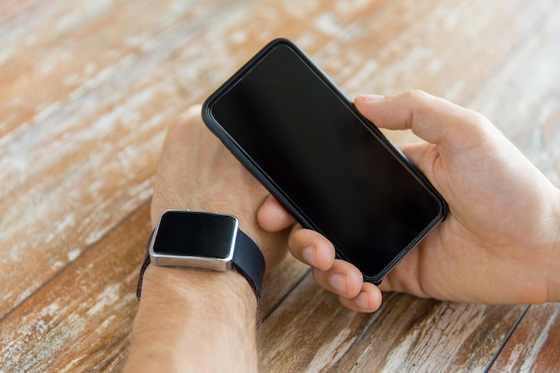 koncepcja biznesu, technologii i ludzi - zbliżenie męskiej ręki trzymającej inteligentny telefon i noszącej zegarek w domu