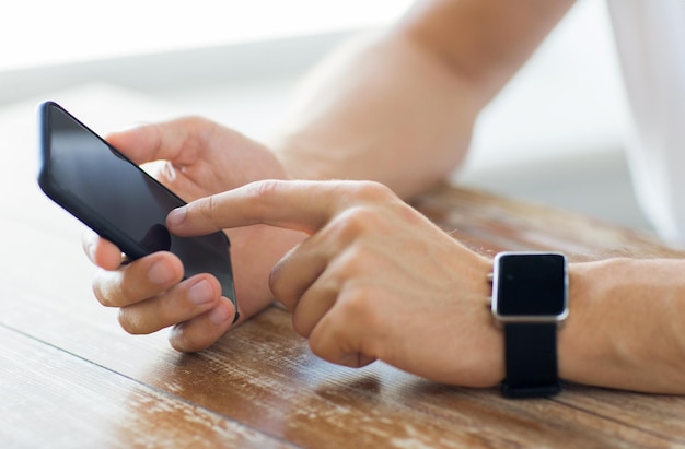 koncepcja biznesu, technologii i ludzi - zbliżenie męskiej ręki trzymającej inteligentny telefon i noszącej zegarek w domu