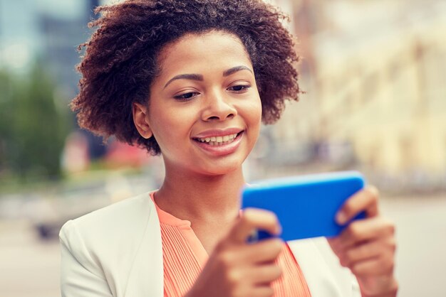 koncepcja biznesu, technologii, komunikacji i ludzi - młoda uśmiechnięta afroamerykańska bizneswoman z wiadomością czytającą smartfon na ulicy miasta