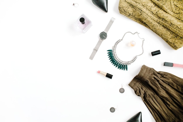 Zdjęcie koncepcja bloga piękności. kobiece ubrania i akcesoria: zielona spódnica i sweter, zegarki, naszyjnik, szminka, buty, okulary przeciwsłoneczne na białym tle. płaski świeckich, widok z góry modne tło kobiece moda.