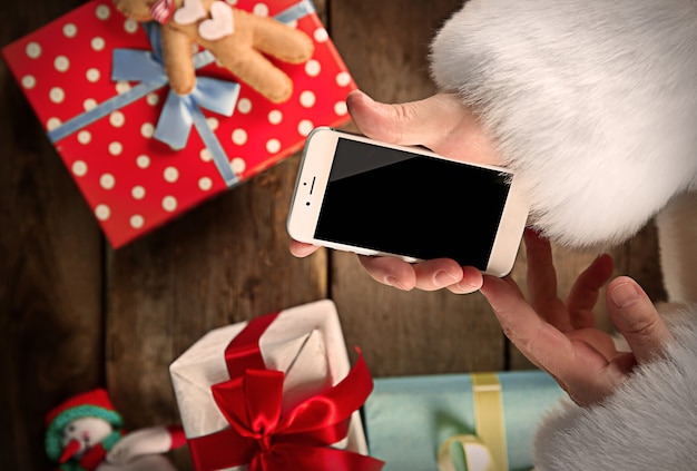 Koncepcja Bożego Narodzenia. Święty Mikołaj z inteligentnym telefonem w rękach z bliska