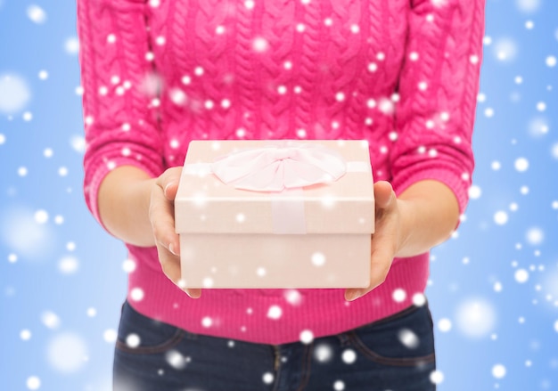 Koncepcja Bożego Narodzenia, Wakacji I Ludzi - Zbliżenie Kobiety W Różowym Swetrze Trzymającym Pudełko Na Niebieskim Tle Z Zaśnieżonym Niebieskim Tłem Ze śniegiem