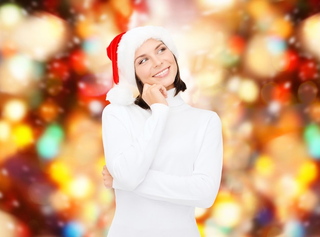 Zdjęcie koncepcja bożego narodzenia, wakacji, zimy, szczęścia i ludzi - myśląca i uśmiechnięta kobieta w kapeluszu pomocnika świętego mikołaja na tle czerwonych świateł