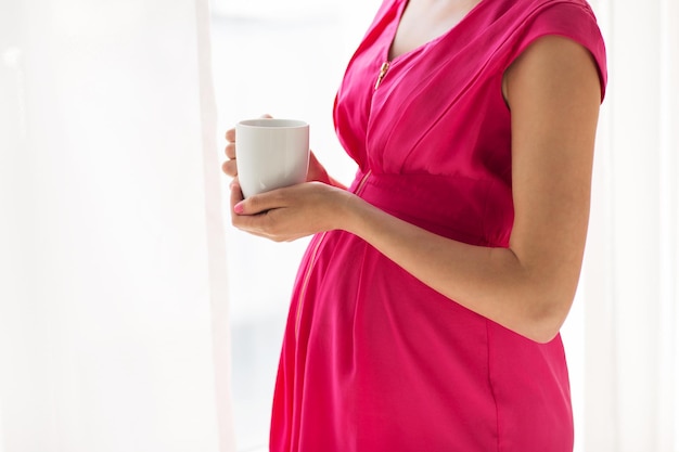 koncepcja ciąży, napojów, odpoczynku, ludzi i oczekiwania - zbliżenie kobiety w ciąży z filiżanką picia herbaty w domu