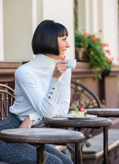 Koncepcja dla smakoszy Uwielbia słodycze Kobieta atrakcyjna elegancka brunetka je tort dla smakoszy kawiarnia taras tło Przyjemny czas i relaks Pyszne ciasto dla smakoszy Dziewczyna relaks kawiarnia z ciastem deser