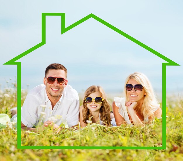 koncepcja domu, szczęścia i nieruchomości - szczęśliwa rodzina w okularach przeciwsłonecznych leżąca na trawie z ilustracją w kształcie domu