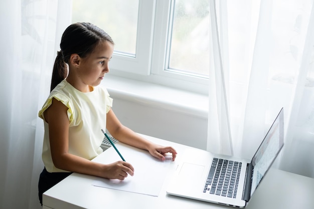 koncepcja domu, wypoczynku, technologii i internetu - mała studentka z laptopem w domu, mała dziewczynka używa czatu wideo