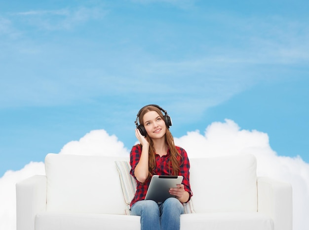 Zdjęcie koncepcja domu, wypoczynku, technologii i szczęścia - uśmiechnięta nastolatka siedząca na kanapie ze słuchawkami i komputerem typu tablet pc