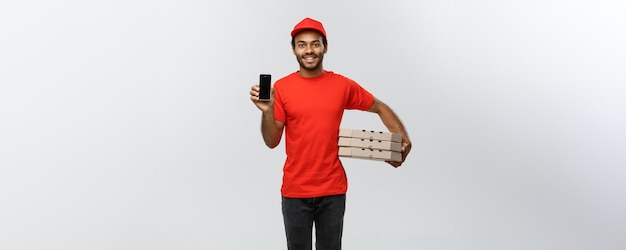 Koncepcja dostawy portret przystojny afroamerykanin dostawa mężczyzna lub kurier z pudełkiem pizzy pokazując telefon komórkowy na ciebie, aby sprawdzić kolejność na białym tle na szarym tle studio miejsce kopiowania
