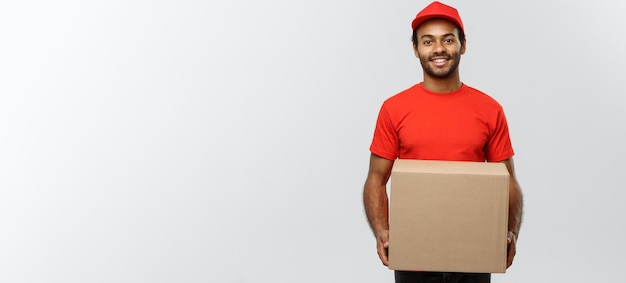 Koncepcja dostawy portret szczęśliwego afroamerykańskiego dostawcy w czerwonym suknie, trzymającego pakiet pudełkowy