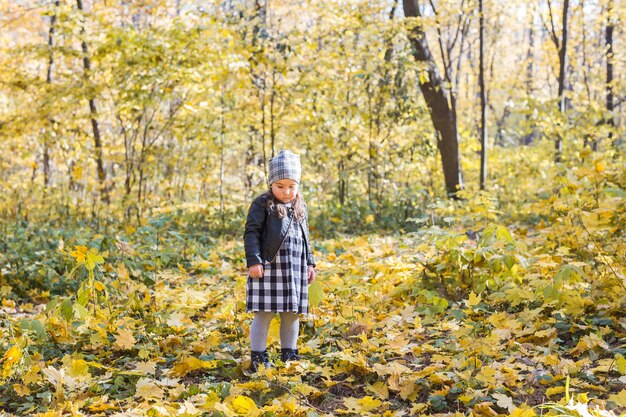 Koncepcja dzieci, jesień i rodzina - mała dziewczynka bawi się opadłymi liśćmi w parku.