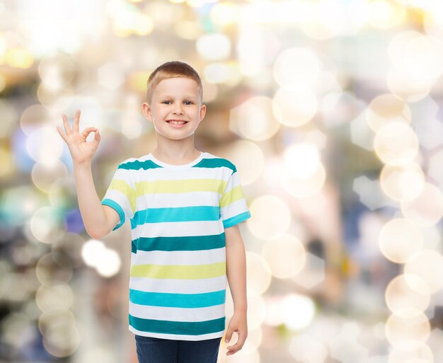 Zdjęcie koncepcja dzieciństwa, gestu, wakacji i ludzi - uśmiechnięty mały chłopiec w zwykłych ubraniach, który wykonuje gest ok nad błyszczącym tłem