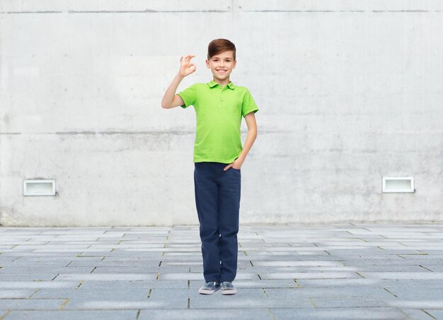 koncepcja dzieciństwa, mody, reklamy i ludzi - szczęśliwy chłopiec w białej koszulce i dżinsach pokazujący znak ręki ok na tle miejskiej ulicy