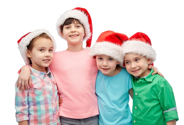 koncepcja dzieciństwa, świąt Bożego Narodzenia, wakacji, przyjaźni i ludzi - grupa szczęśliwych uśmiechniętych małych dzieci w czapkach mikołaja przytulających się
