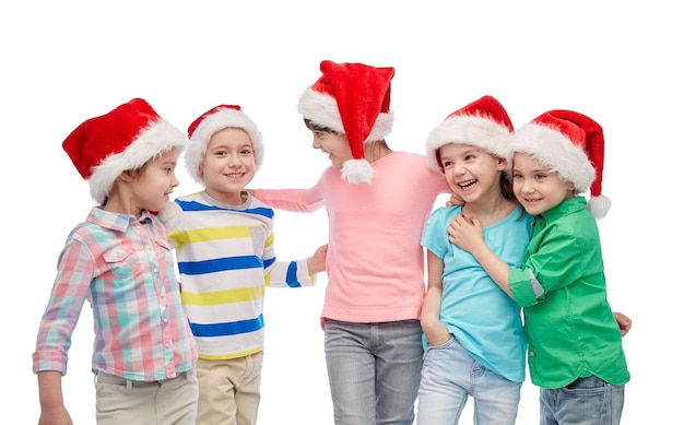 koncepcja dzieciństwa, świąt Bożego Narodzenia, wakacji, przyjaźni i ludzi - grupa szczęśliwych uśmiechniętych małych dzieci w czapkach mikołaja przytulających się