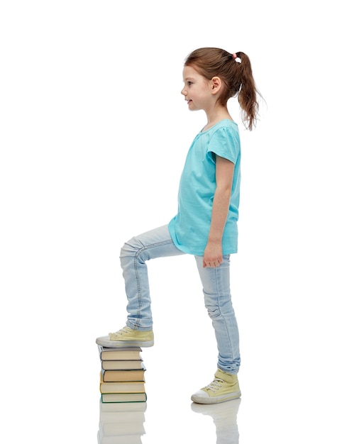 koncepcja dzieciństwa, szkoły, edukacji i ludzi - szczęśliwa mała dziewczynka nadepnęła na stos książek
