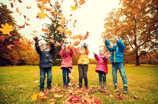Zdjęcie koncepcja dzieciństwa, wypoczynku, przyjaźni i ludzi - grupa szczęśliwych dzieci bawiących się jesiennymi liśćmi klonu i bawiących się w parku