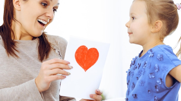 Koncepcja dzień matki. Córka gratuluje mamie i daje jej pocztówkę w kształcie czerwonego serca. Mama i dziewczyna szczęśliwa uśmiechnięta i przytulająca. Rodzinna zabawa i wakacje.