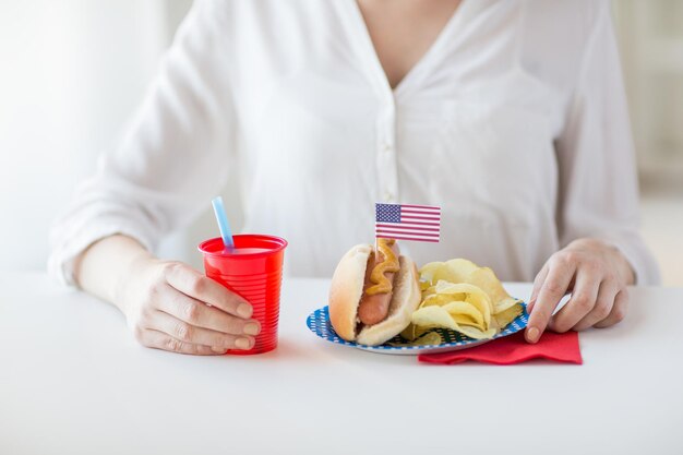 koncepcja dzień niepodległości, świętowanie, patriotyzm i święta - zbliżenie kobiety jedzącej hot doga z dekoracją flagi amerykańskiej i chipsami ziemniaczanymi, pijące sok i świętujące 4 lipca na imprezie domowej