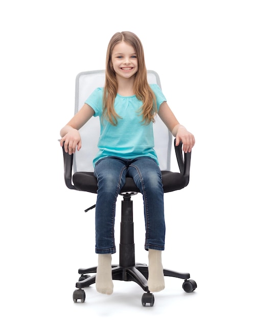 koncepcja edukacji, biura i szczęśliwych ludzi - uśmiechnięta dziewczynka siedzi na dużym krześle biurowym
