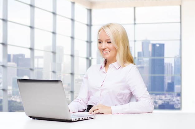 koncepcja edukacji, biznesu i technologii - uśmiechnięta bizneswoman z laptopem nad pokojem biurowym z tłem okna z widokiem na miasto
