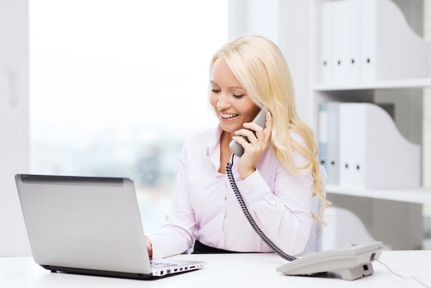 Zdjęcie koncepcja edukacji, biznesu, komunikacji i technologii - uśmiechnięta kobieta lub studentka z laptopem dzwoniąca na telefon w biurze