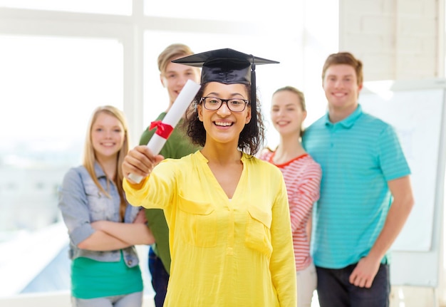 koncepcja edukacji i ludzi - uśmiechnięta studentka z dyplomem i narożnikiem i przyjaciółmi z tyłu